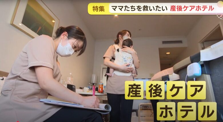産後ケアホテルの客室で、助産師が赤ちゃんを抱っこしながらケアを行い、もう一人の助産師が記録をつけている様子。