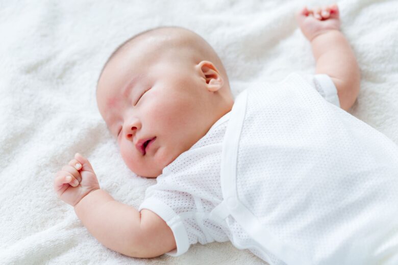 白い服を着て布の上で気持ちよさそうに眠る赤ちゃん