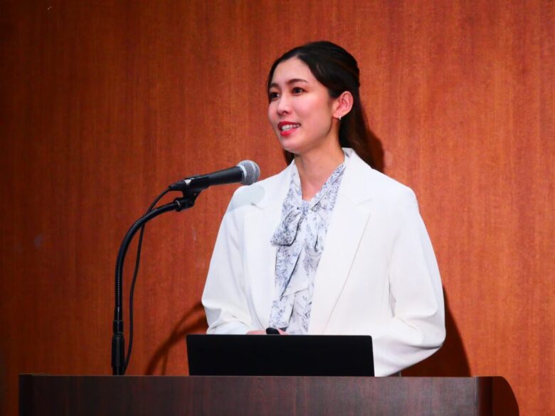 代表の高橋が壇上でマイクに向かって発表している様子
