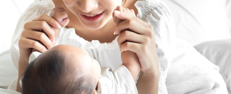 赤ちゃんの両手を頬に当てて微笑む母親