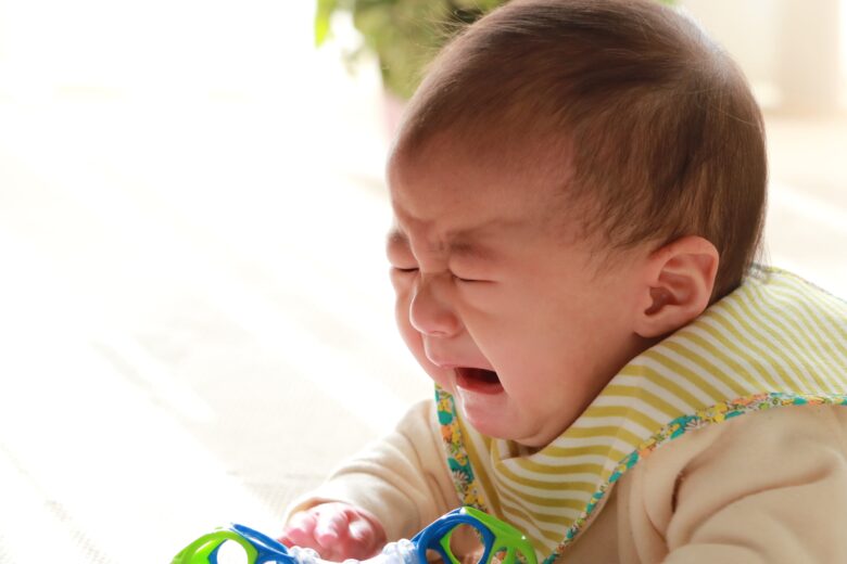 おもちゃを握りながら泣いている赤ちゃん
